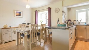 Een moderne keuken met houten kastjes, een eethoek met een tafel en stoelen, en een klein kookeiland met een spoelbak.
