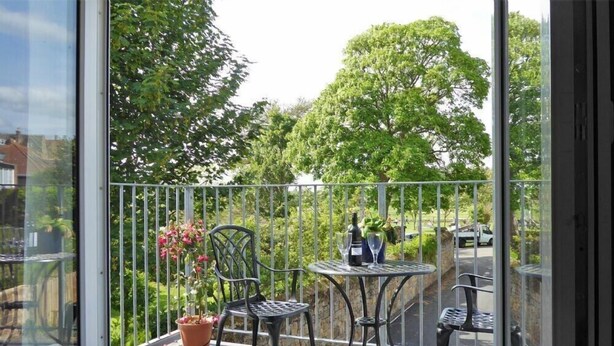 Een balkon met twee metalen tafels en stoelen, een potplant en een fles wijn.