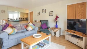Een woonkamer met een bank, salontafel, televisie en een kleine keuken in de achtergrond.