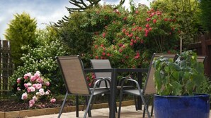 Eine Terrasse im Freien mit Tisch und Stühlen, umgeben von üppiger Vegetation und blühenden Pflanzen.
