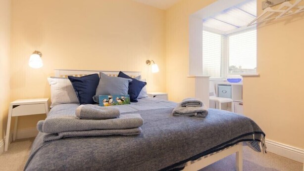 Ein Schlafzimmer mit Bett, Kissen, Nachttisch, Fenster und Handtuchhalter.