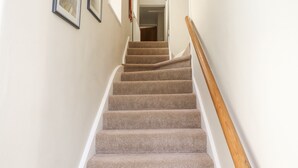 A carpeted staircase with a wooden handrail, leading to a room with a door. - The Hollies (Bamburgh)