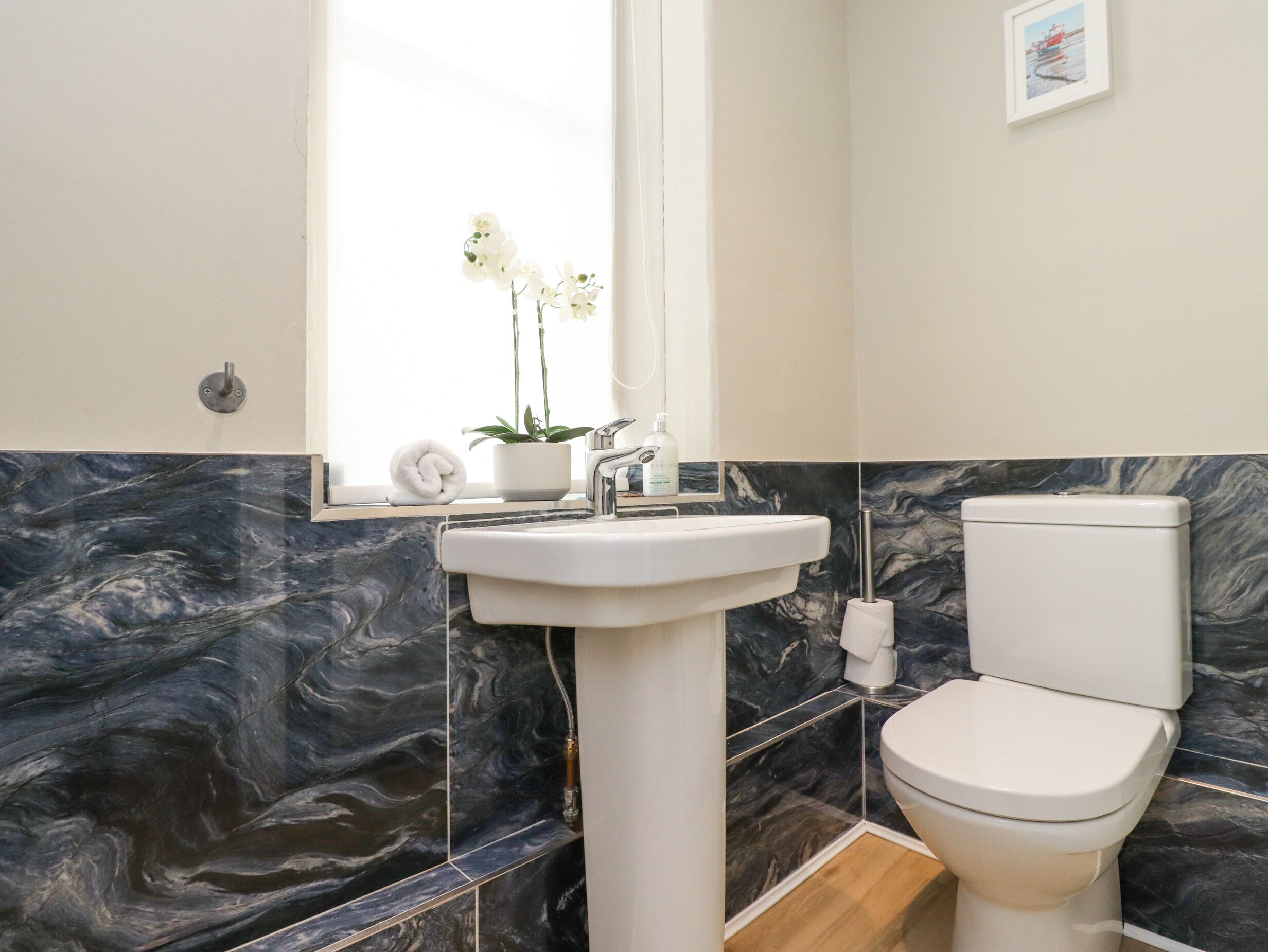 Une salle de bain avec un lavabo blanc, des toilettes et une fenêtre ornée d’une orchidée en pot.