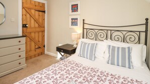 A bedroom with a bed, a dresser, a wooden door, and two framed pictures on the wall. - The Hollies (Bamburgh)