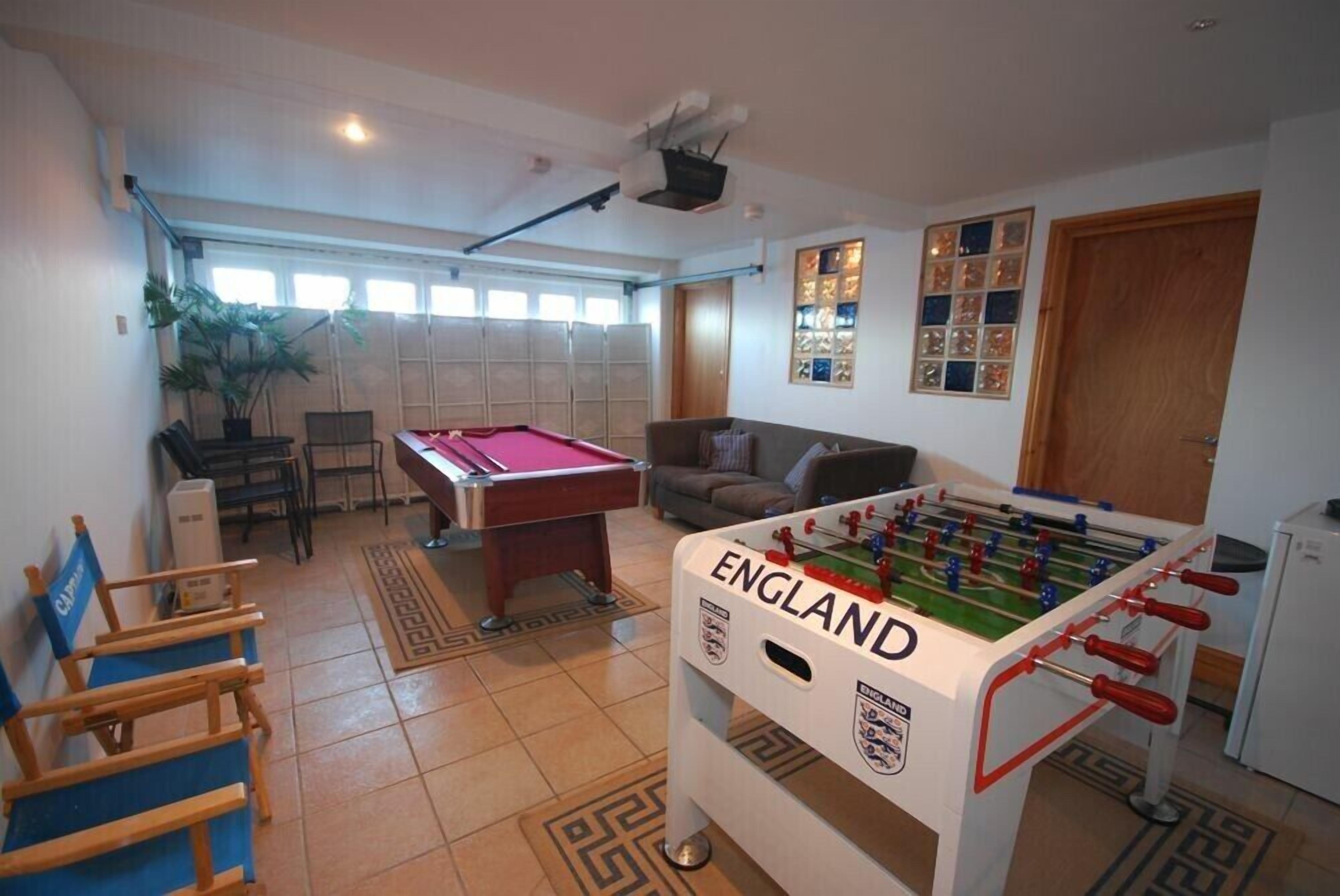 Una habitación con mesa de futbolín con la etiqueta 'ENGLAND', mesa de billar, sofá y zona de comedor con sillas y una mesa.