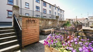 A wooden staircase leading to a building with a stone wall and a flower bed with purple flowers. - Farne Lookout (Seahouses)