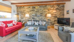 A living room with a stone wall, two sofas, a coffee table, a TV, and a bookshelf. - Farne Lookout (Seahouses)