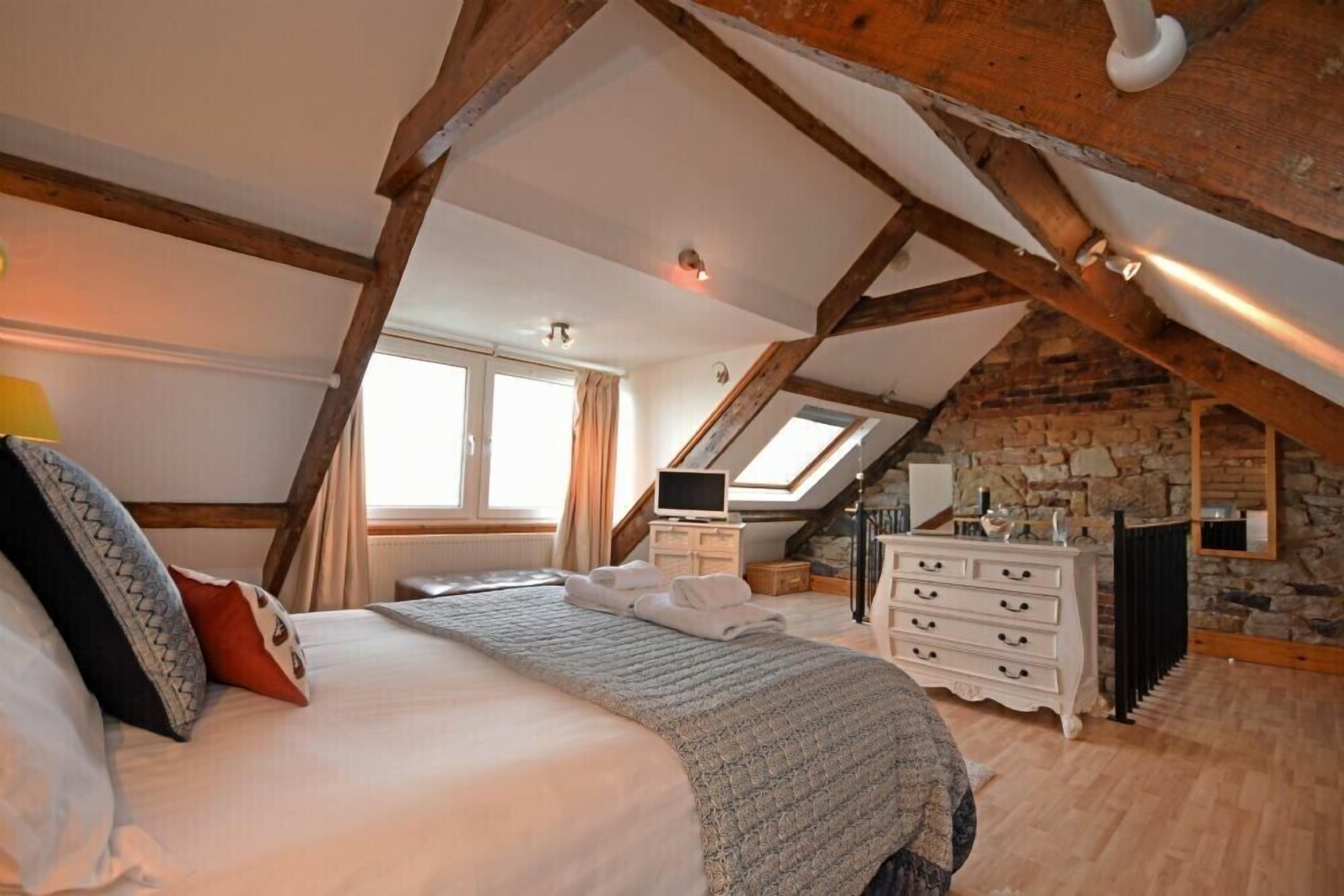 Een slaapkamer met een groot bed, een dressoir, een televisie en een stenen muur.