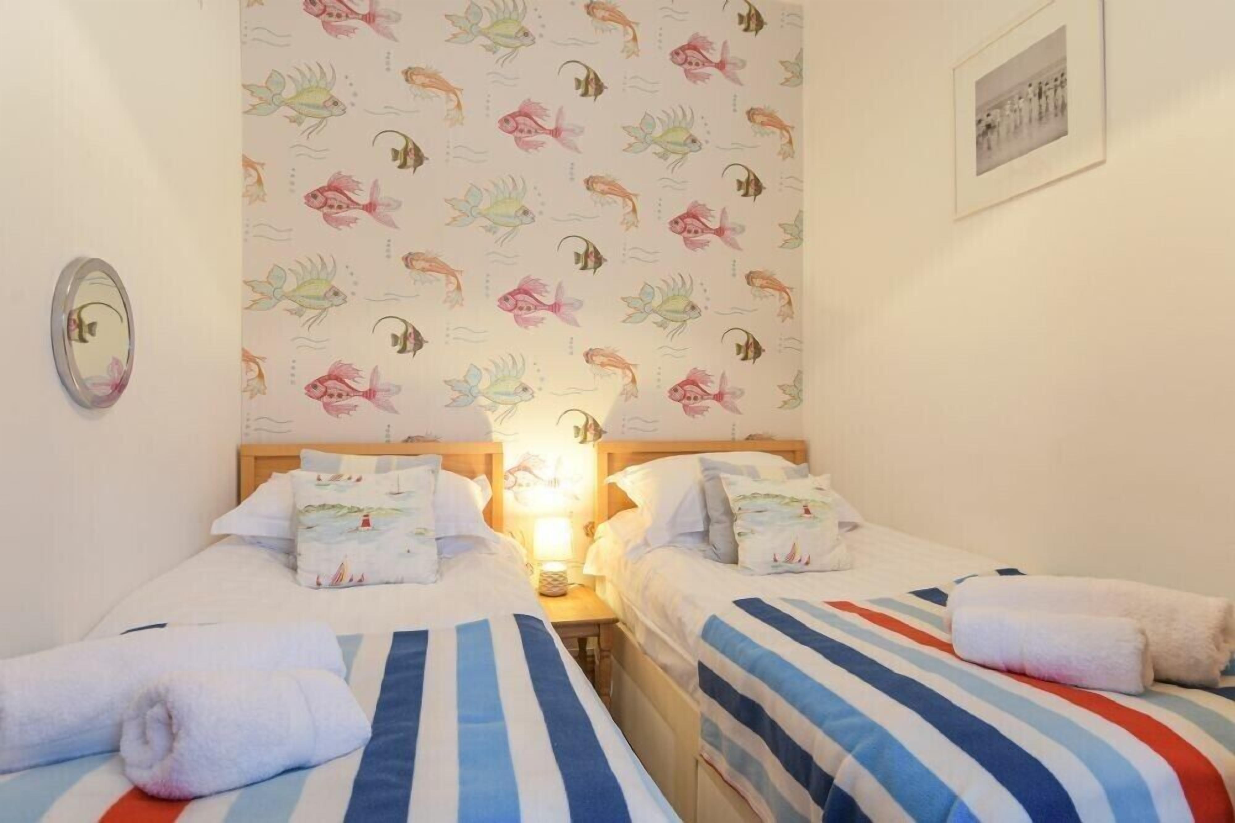 Une chambre avec deux lits, une literie à rayures, un mur décoré d’un motif de poissons, une lampe de chevet et un tableau encadré au mur.