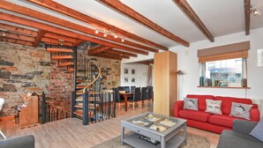 A spacious living area with exposed wooden beams, a stone wall, a spiral staircase, a red sofa, and a glass coffee table. - Farne Lookout (Seahouses)