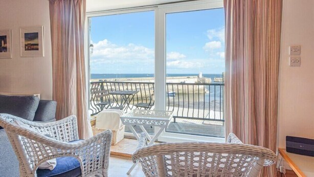 A balcony with wicker furniture, a view of the sea, and a glass door leading to the balcony. - Farne Lookout (Seahouses)