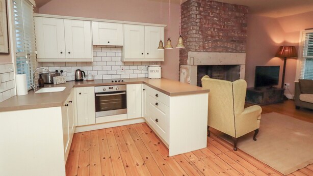 Een moderne keuken met witte kasten, een ingebouwde oven en een open haard van baksteen.