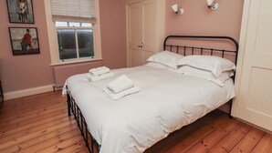 Een netjes opgemaakt bed met witte lakens en handdoeken, een raam met zonwering, een radiator en een deur met een witte omlijsting.