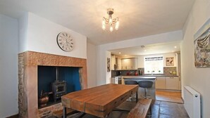 A cozy kitchen with a stone fireplace, wooden table, and modern lighting. - Beach Retreat (Seahouses)