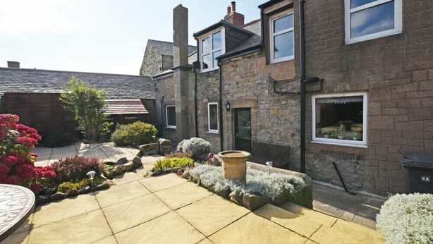A courtyard with stone buildings, a paved area, and various plants. - Beach Retreat (Seahouses)