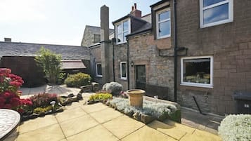 A courtyard with stone buildings, a paved area, and various plants.