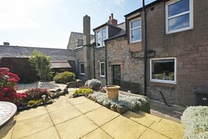 A courtyard with stone buildings, a paved area, and various plants. - Beach Retreat (Seahouses)