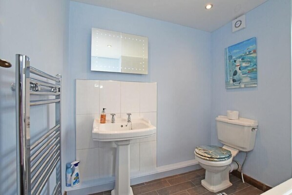 A bathroom with a white sink, a mirror with lights, a toilet, and a painting on the wall. - Beach Retreat (Seahouses)