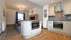 A modern kitchen with built-in appliances, a dining area with a bench, and a fireplace. - Beach Retreat (Seahouses)