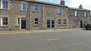 A row of stone buildings with multiple doors and windows, likely residential or small commercial properties. - Beach Retreat (Seahouses)