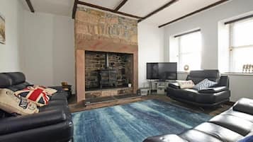 A living room with a stone fireplace, leather sofas, a television, and a large window.