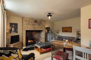 A cozy living room with a fireplace, a television, a dining table with chairs, and a sofa. - Sandpiper (Alnwick)