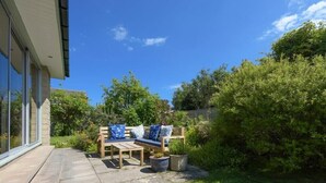 A patio with a wooden bench and table, surrounded by greenery and a building with large windows. - Spuggies Rest (Alnwick)