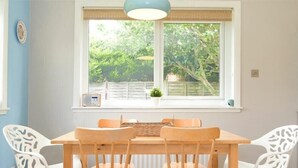 A dining area with a table and chairs, a window with a view of greenery, and a ceiling light fixture. - Spuggies Rest (Alnwick)