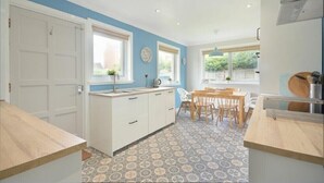 A compact kitchen with white cabinets, a wooden countertop, and patterned floor tiles. - Spuggies Rest (Alnwick)