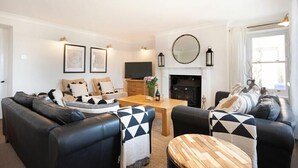 A living room with a fireplace, a TV, and a dining area with a wooden table and chairs. - Cargoes (Alnwick)