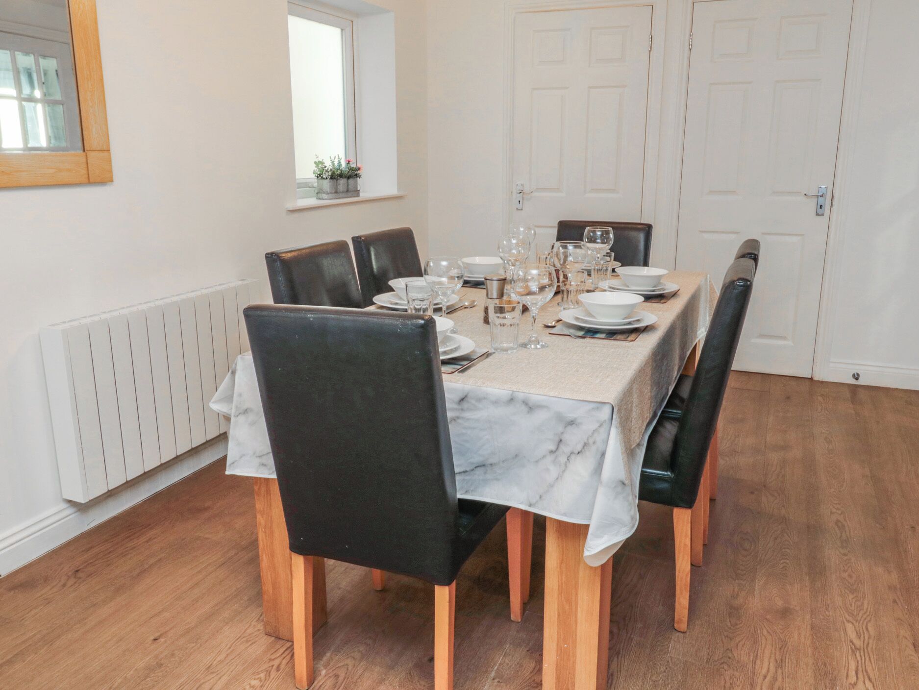 Un espace repas avec une table en marbre, des chaises noires et une nappe blanche.