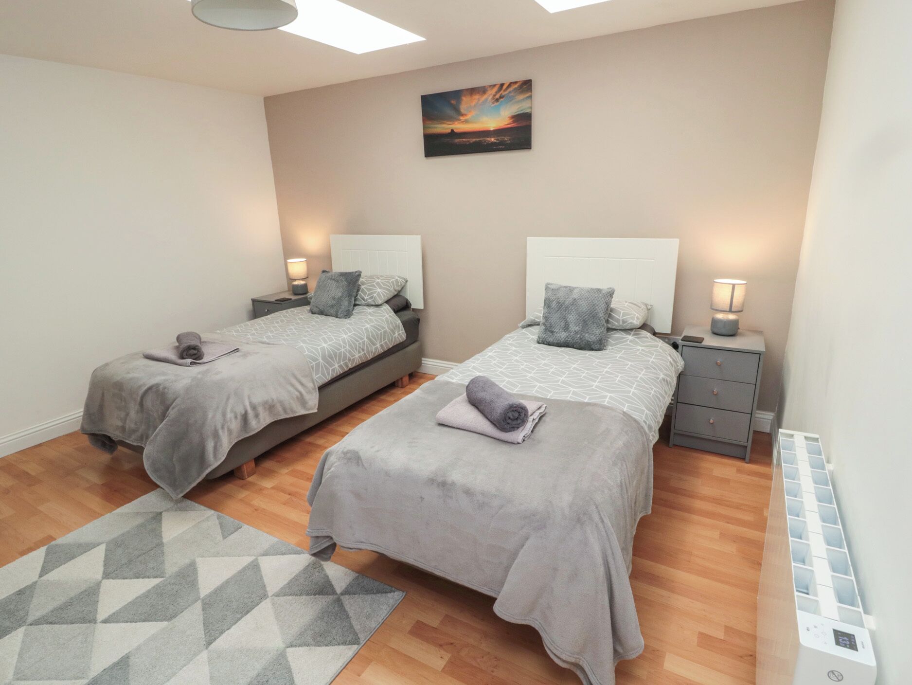 Un dormitorio con dos camas, cada una con una mesita de noche, una lámpara y una almohada. Hay un cuadro en la pared y una alfombra estampada en el suelo.