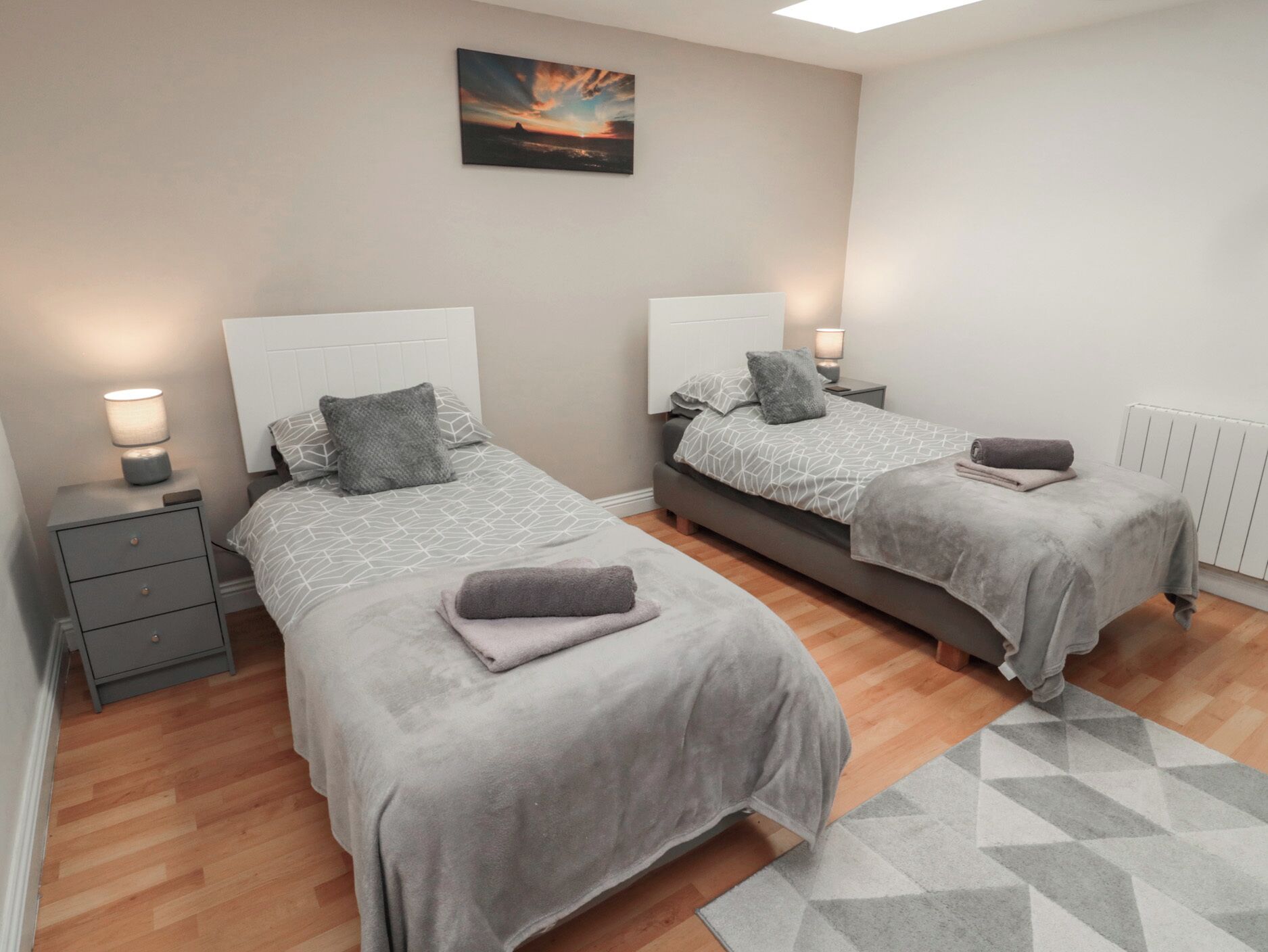 Quarto com duas camas, cada uma com cabeceira, mesas de cabeceira e luminárias. Um quadro está na parede acima das camas.