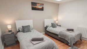 A bedroom with two beds, each with a headboard, bedside tables, and lamps. A painting is on the wall above the beds. - Butcher's Retreat (Seahouses)