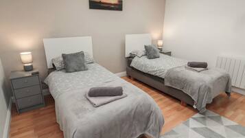 Quarto com duas camas, cada uma com cabeceira, mesas de cabeceira e luminárias. Um quadro está na parede acima das camas.