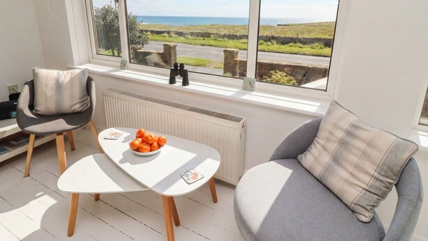 A cozy room with a view of the sea, a table with a bowl of fruit, and two chairs. - Dell Point (Chathill)