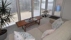 A sunlit room with a sofa, a wooden table, and a potted plant. - Dell Point (Chathill)