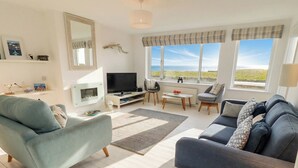 A modern living room with a sofa, armchair, TV, and a view of the sea. - Dell Point (Chathill)
