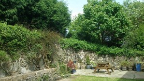 Un muro in pietra con piante in vaso e un'altalena in legno in un giardino.