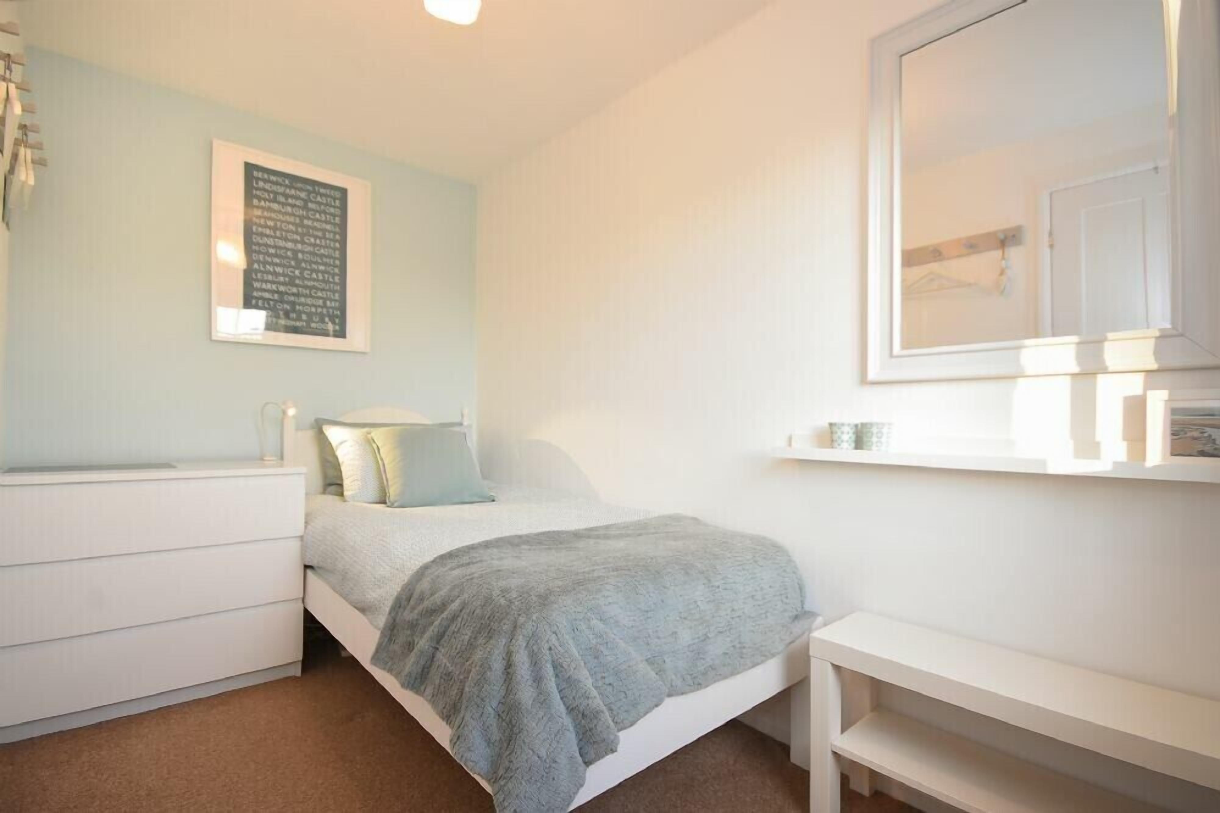 Un dormitorio con cama, mesita de noche, cómoda, espejo y un cuadro enmarcado en la pared.