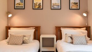 Camera d'albergo con due letti, ciascuno con biancheria da letto bianca e cuscini decorativi. Sopra i letti, si vedono quadri incorniciati e sono presenti delle lampade ai comodini.