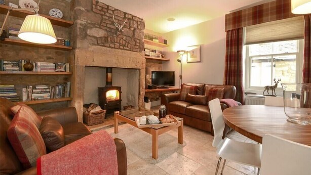 Ein gemütliches Wohnzimmer mit Kamin aus Stein, Ledersofas, einem Holztisch und einem Fernseher.