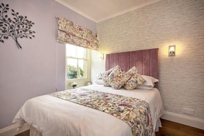 A bedroom with a bed, floral bedding, a decorative wall piece, and a window with a view.