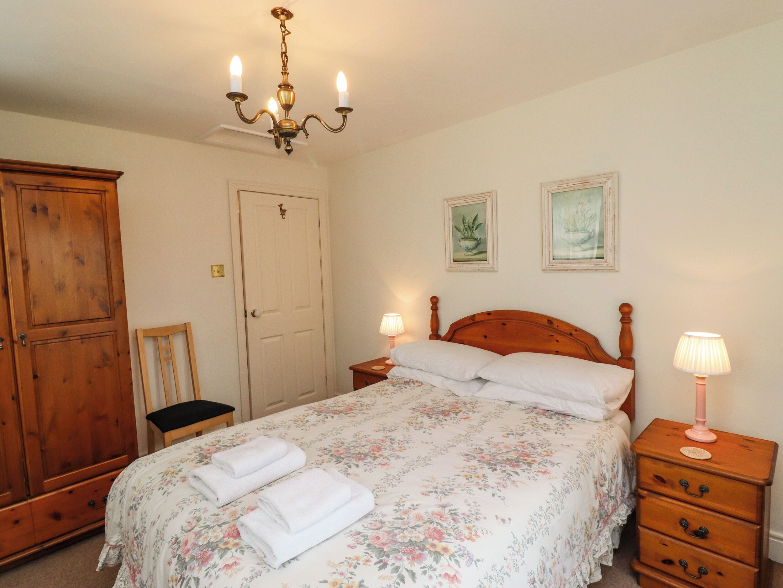 Une chambre à coucher avec un lit en bois, deux tables de chevet, une armoire en bois et un lustre.