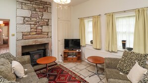 Ein Wohnzimmer mit Kamin aus Stein, einem Fernseher, zwei Sesseln und einem gemusterten Teppich.