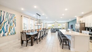 A modern kitchen with a large island, dining area with chairs, and a view of the living room. - Encore Luxe 9 BR, Home Theater, Private Pool & Spa (Four Corners)