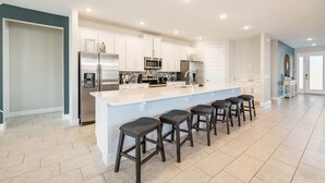 A modern kitchen with a central island, stainless steel appliances, and a bar stool seating arrangement. - Encore Luxe 9 BR, Home Theater, Private Pool & Spa (Four Corners)