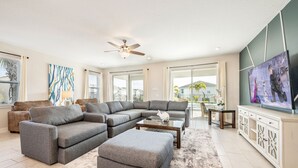 A spacious living room with a sectional sofa, ottoman, and a flat-screen TV on a cabinet. - Encore Luxe 9 BR, Home Theater, Private Pool & Spa (Four Corners)