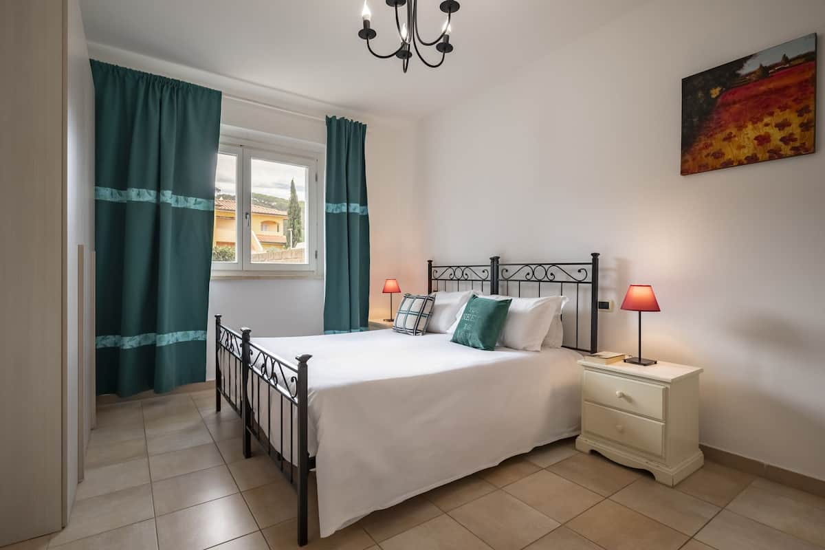 Un dormitori amb llit, tauells de nit, un penjoll, cortines i un quadre a la paret.