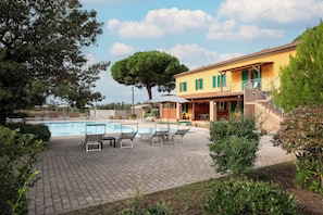 A poolside area with lounge chairs and a building with green shutters.